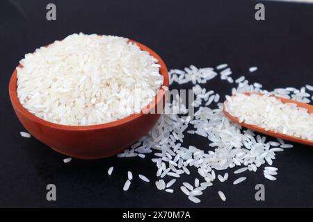 Rice in a wooden bowl and a wooden spoon partially spread out, with a close up view of the dark background. Stock Photo