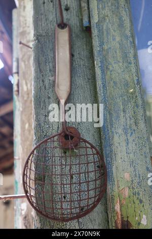 very old rusty handle colander strainer hanging on the wall Stock Photo