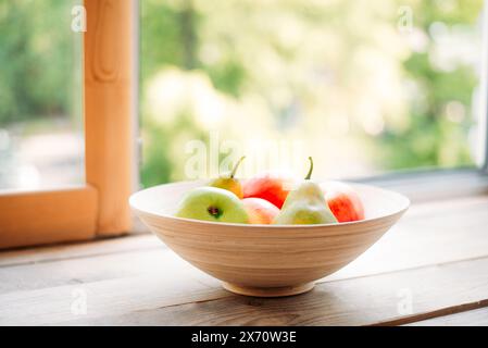 apples and pears on a windowsill in a wooden plate. summer and fresh fruits. Stock Photo