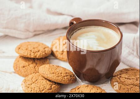 A cup of aromatic coffee cappuccino with Oatmeal cookies. Morning rays and latte for breakfast in a beautiful brown cup. Wooden background Stock Photo