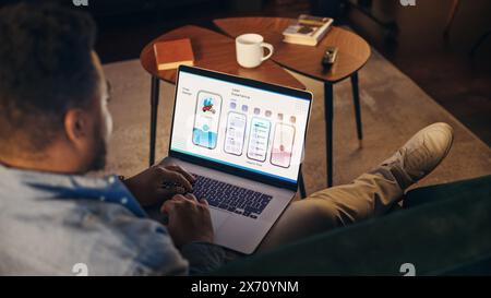 Young African American Men Working On Laptop Computer, Sitting on The Sofa in Stylish Loft Apartment. Creative Designer is Developing UX, UI for New Project, Preparing Presentation For the Clients. Stock Photo