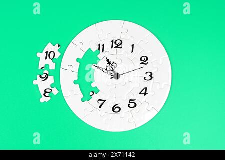 Jigsaw puzzle in the form of a clock with two missing pieces set aside on a green backdrop. Time related concept. Stock Photo