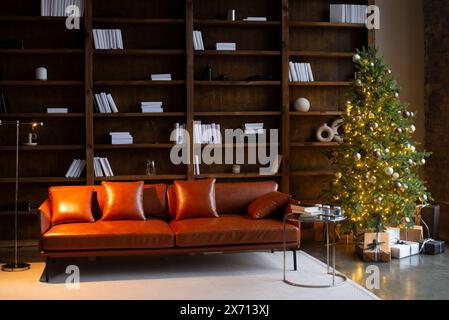 Room interior with leather brown sofa, christmas tree and brown shelves with books in loft style. Stock Photo