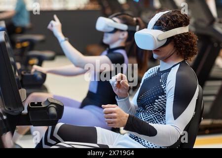 Side view portrait of young man on exercise bikes in gym wearing VR headset for immersive training simulation copy space Stock Photo