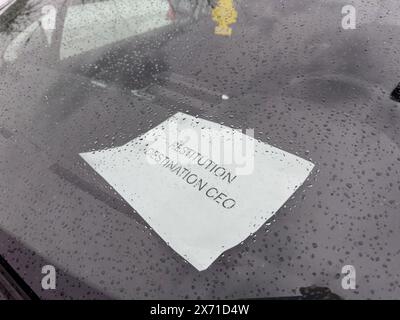 A paper notice with Restitution Destination CEO on a car windshield covered in raindrops, showing a rainy day and droplets on the glass - car dealership Stock Photo