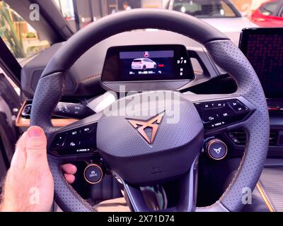 Paris, France - Feb 7, 2024: Point of view of a male hand on the steering wheel of a new Seat Cupra model electric car, featuring multiple buttons and a computer display dashboard showcasing advanced vehicle controls Stock Photo