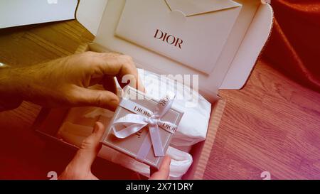 Paris, France - Jun 5th, 2020: Hands delicately unbox a Dior gift, revealing a beautifully packaged item with a Dior ribbon, amidst elegant packaging on a wooden table Stock Photo