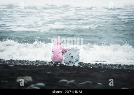 Tourist woman by blue iceberg piece on the black sandy shore of Diamond Beach, Iceland Stock Photo