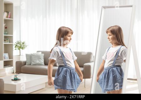 Little girl holding her skirt and looking into a mirror in a living room Stock Photo