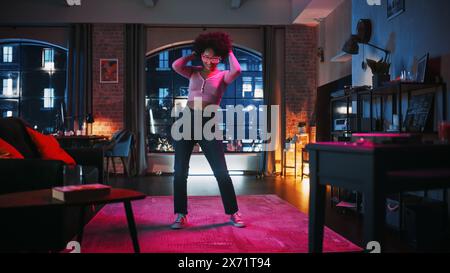 Portrait of Diverse Multiethnic Young Black Female Dancing in Futuristic Neon Glowing Glasses, Having a Party at Home in Loft Apartment. Recording Funny Viral Videos for Social Media. Stock Photo