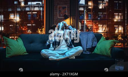 Cinematic Portrait of a Young Stylish Female with Short Hair Putting On Virtual Reality Headset. Creative Woman Sitting on a Sofa at Home in the Evening, Playing VR Video Games. Wide Shot. Stock Photo