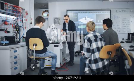 University Robotics Class. White Male Teacher Explaining Engineering to Students And Using Robot Arm. Diverse Group of Young Engineers Sitting at University. Computer Science Education Concept. Stock Photo