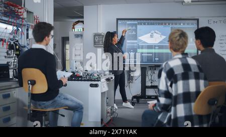 Teacher is Explaining Principles of Working With Robotic Hand, Showing Examples on Big Screen at Modern University. Teenagers Brainstorming and Asking Questions. Robotic Engineering Concept. Stock Photo