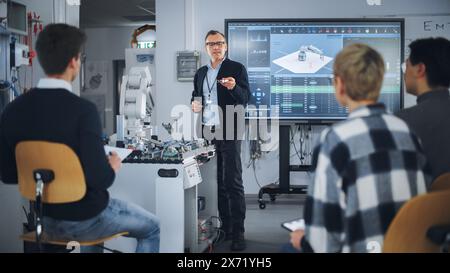 Teacher Holding Microchip for Futuristic Equipment During the Lesson while Robotic Arm Moving Nearby. Diverse Group of Young Engineers Sitting at University. Computer Science Education Concept Stock Photo