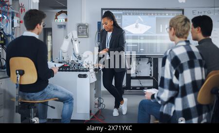 University Robotics Class: Black Teacher Explaining Engineering to Students Using Robot Arm. Diverse Group of Young Engineers Programming Robotic Hand. Computer Science Education Build, Design, Learn Stock Photo