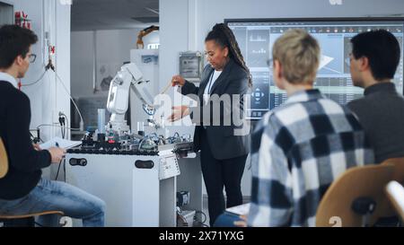 Black Teacher and Diverse Group of Young Students Brainstorming at University Robotics Class. People Discussing with their Educator while Using Robot Arm. Computer Science Education, Design, Learn. Stock Photo