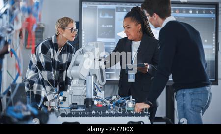 University Robotics Class: Black Teacher Explaining Engineering to Students And Using Robot Arm. Diverse Group of Young Engineers Brainstorming while Programming. Computer Science Education Concept. Stock Photo