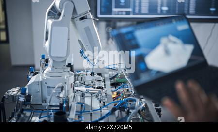 Black Female Engineer Using Laptop for Programming Robotic Arm At the Futuristic Advanced Factory. New Generation Technology in Automatic Manufacturing Industry Concept. Cropped View. Stock Photo