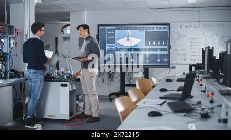 Team of Future Robotics Engineers Working on Robot Arm Design And Discussing Technical Capabilities of Futuristic Device. Students Using Tablet Computers. Digital Technology and Success Concept. Stock Photo
