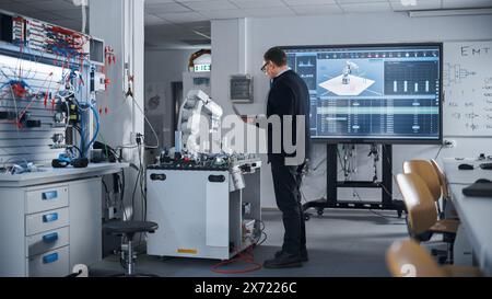 Male Engineer Holding Laptop, Moving Bionic Limb With Written Code And Analysing Results on Big Screen. Modern Equipment and New Era in Computer Science and Robotics Industry Concept. Stock Photo