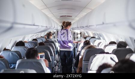 Interior of airplane with passengers on seats and female traveler walking the aisle. Commercial economy flight service concept Stock Photo