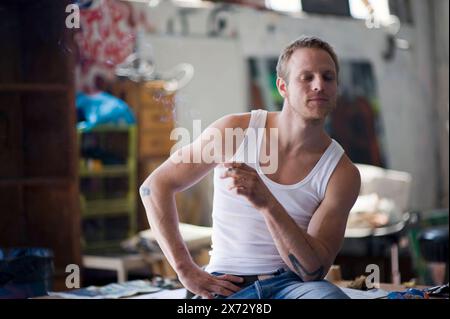 Young Adult Male Enjoying a Joint Young adult male enjoying a Joint with Hashish / Pot while sitting on a table inside an Art studio. Rotterdam, Netherlands. Rotterdam Kraakpand Merwehaven Zuid-Holland Nederland Copyright: xGuidoxKoppesxPhotox Stock Photo