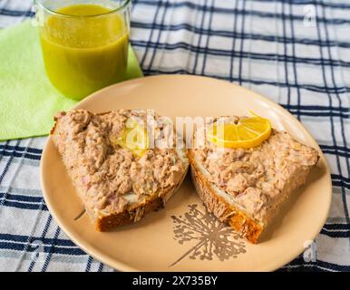 Two slice bread with tuna fish spread, lemon, green smoothie in glass on table, closeup. Breakfast or snack. Stock Photo