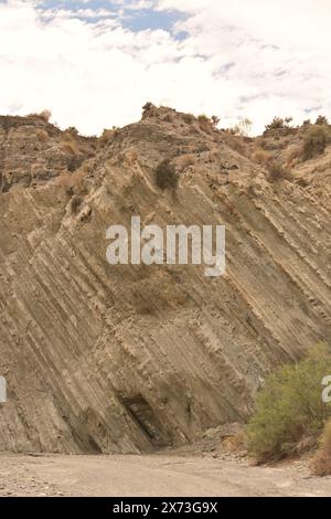 Steep rocky cliff with visible striations and sparse vegetation, illustrating the rugged geological features of the landscape Stock Photo