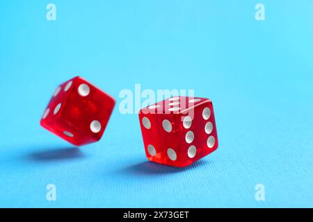 Two red game dices falling on light blue background, closeup Stock Photo