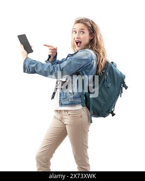 Excited young woman tourist traveler pointing at the screen of her smartphone, wearing a backpack on her shoulders, isolated on a white background. Co Stock Photo