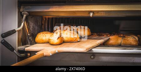 Freshly baked loaves of bread on a wooden board using a wooden pusher. Stock Photo