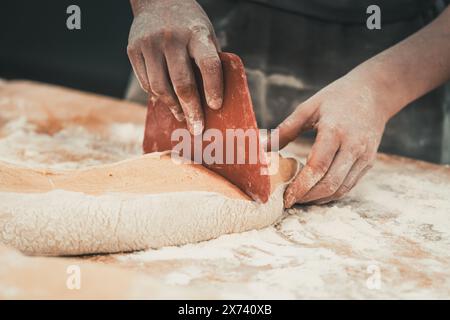 A female baker divides pieces of dough with a dough cutter. Stock Photo