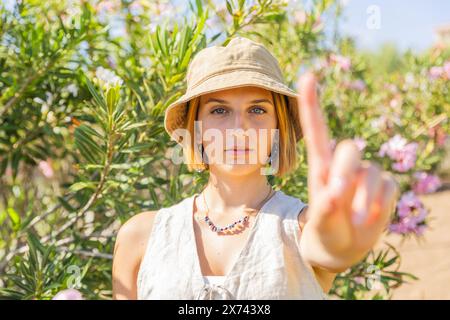 A serious woman wearing a hat and necklace is pointing her finger in the air. Stock Photo