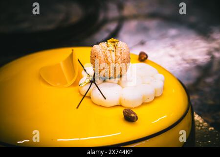 Tart with a yellow glaze, macaron, cookie, chocolate and gold decoration, dark background, close up. Stock Photo