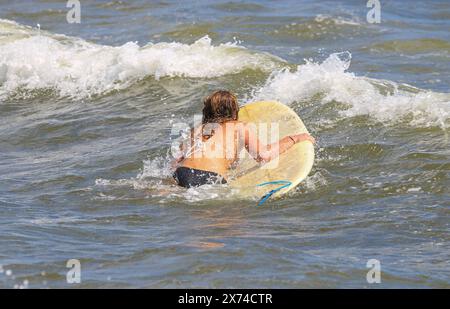 Rear view of a girl in a biklini paddling on a surfboard to get out further in the ocean Stock Photo