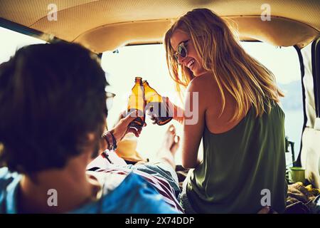Travel, couple and car for cheers and beer, boot and happy in vehicle for road trip and vacation. Smile, sunset or date for man and female person in Stock Photo