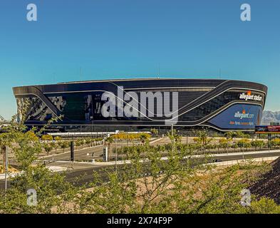 Las Vegas, NV, USA - May 12, 2024: Black Allegiant Stadium closeup with airline sign under blue sky. Empty parking and green foliage Stock Photo