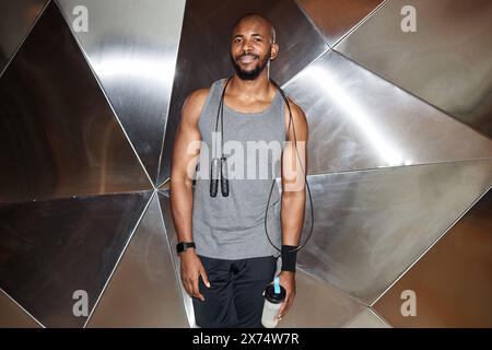Waist up portrait of muscular Black man smiling at camera standing against graphic metal wall in gym, shot with flash Stock Photo