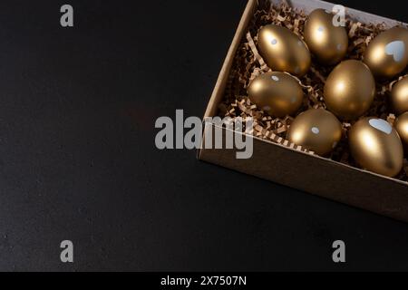 Golden eggs in paper box on dark table. Stock Photo