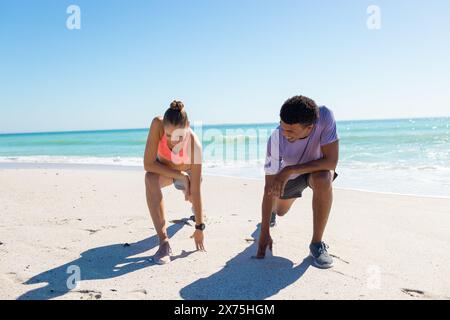 At beach, diverse couple catching breath on sunny day, both looking fit Stock Photo