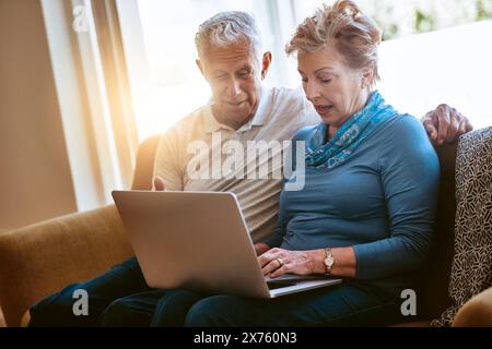Senior couple, typing and relax with laptop on sofa for browsing, online research or email at home. Elderly man and woman discussing finance Stock Photo
