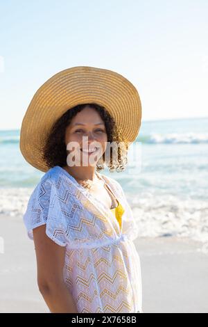 At beach, biracial young woman wearing sun hat, smiling Stock Photo