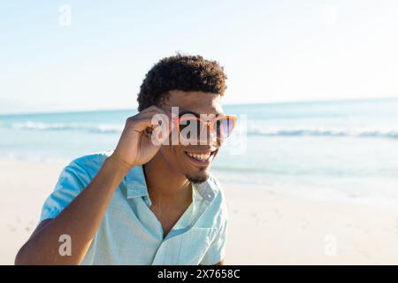 At beach, biracial young man wearing sunglasses, smiling Stock Photo