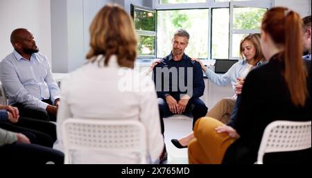 People Consoling Man In Group Therapy Session Stock Photo