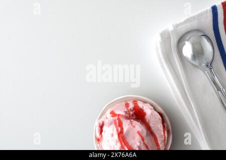 Background with paper cup with scoop of strawberry ice cream decorated with syrup on white table with napkin and spoon. Top view. Stock Photo