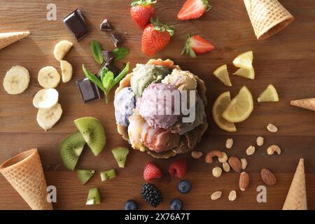 Assorted ice cream scoops on wafer glass on wooden table full of ingredients and cones. Top view. Stock Photo