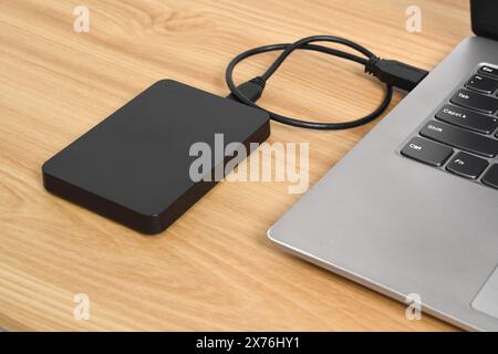 External backup hard disk drive connected to laptop on wooden table. external hard disk connect by USB 3.0 port to laptop Stock Photo