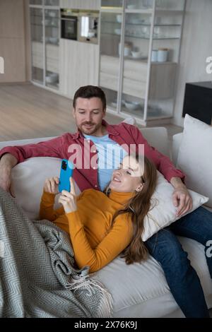 Cheerful woman lying on man knees, holding smartphone, smiling while having videocall with relatives Stock Photo