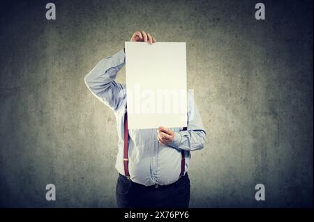 A young chubby man holds a sheet of white paper in front of his face Stock Photo