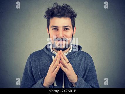 Cunning man clasping hands and planning evil tricky prank or scheming, cheating with sly smile Stock Photo